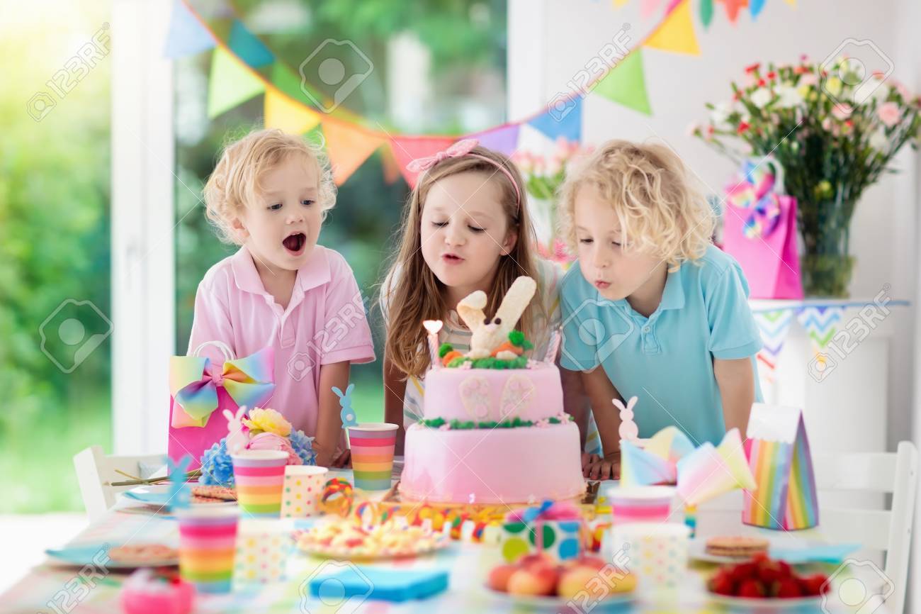 Kids birthday party. Children blow out candles on pink bunny cake. Pastel rainbow decoration and table setting for kids event, banner and flag. - 102743767 Kids birthday party. Children blow out candles on pink bunny cake. Pastel rainbow decoration and table setting for kids event, banner and flag. - 102743767