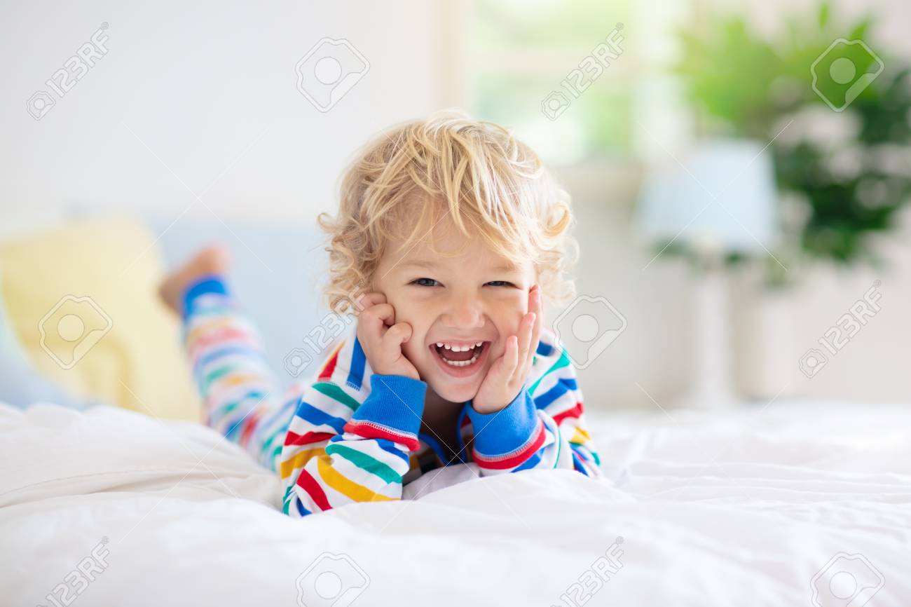 Child playing in bed in white sunny bedroom with window. Kids room and interior design. Baby boy at home. Bedding and textile for children nursery. Kid with toy and book. Nap and sleep time. - 123776408 Child playing in bed in white sunny bedroom with window. Kids room and interior design. Baby boy at home. Bedding and textile for children nursery. Kid with toy and book. Nap and sleep time. - 123776408