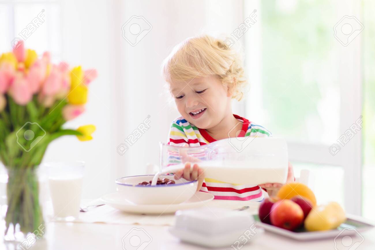 Child having breakfast. Kid drinking milk and eating cereal with fruit. Little boy at white dining table in kitchen at window. Kids eat on sunny morning. Healthy balanced nutrition for young kids. - 126187339 Child having breakfast. Kid drinking milk and eating cereal with fruit. Little boy at white dining table in kitchen at window. Kids eat on sunny morning. Healthy balanced nutrition for young kids. - 126187339