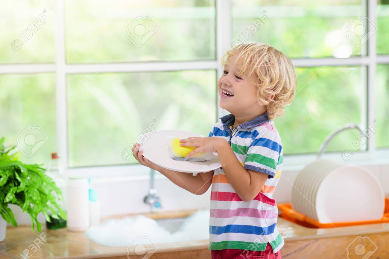 Child washing dishes. Home chores. Kid in white kitchen cleaning plates after lunch at window. - 128867514 Child washing dishes. Home chores. Kid in white kitchen cleaning plates after lunch at window. - 128867514