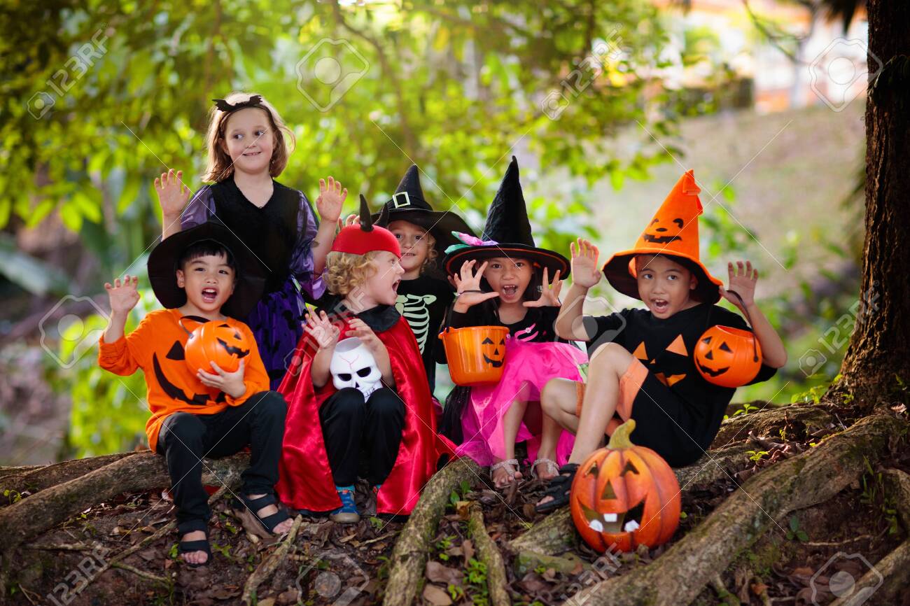 Child in Halloween costume. Mixed race Asian and Caucasian kids trick or treat on suburban street. Little boy and girl with pumpkin lantern and candy bucket. Baby in witch hat. Autumn holiday fun. - 129956240 Child in Halloween costume. Mixed race Asian and Caucasian kids trick or treat on suburban street. Little boy and girl with pumpkin lantern and candy bucket. Baby in witch hat. Autumn holiday fun. - 129956240
