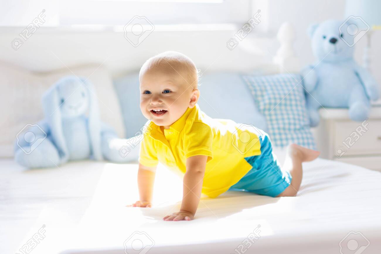 Baby playing on parents bed. Cute funny little boy learning to crawl in white sunny nursery. Infant and toddler room interior. Bedding and toys for kids. Children play at home. Baby bedroom. - 131756975 Baby playing on parents bed. Cute funny little boy learning to crawl in white sunny nursery. Infant and toddler room interior. Bedding and toys for kids. Children play at home. Baby bedroom. - 131756975