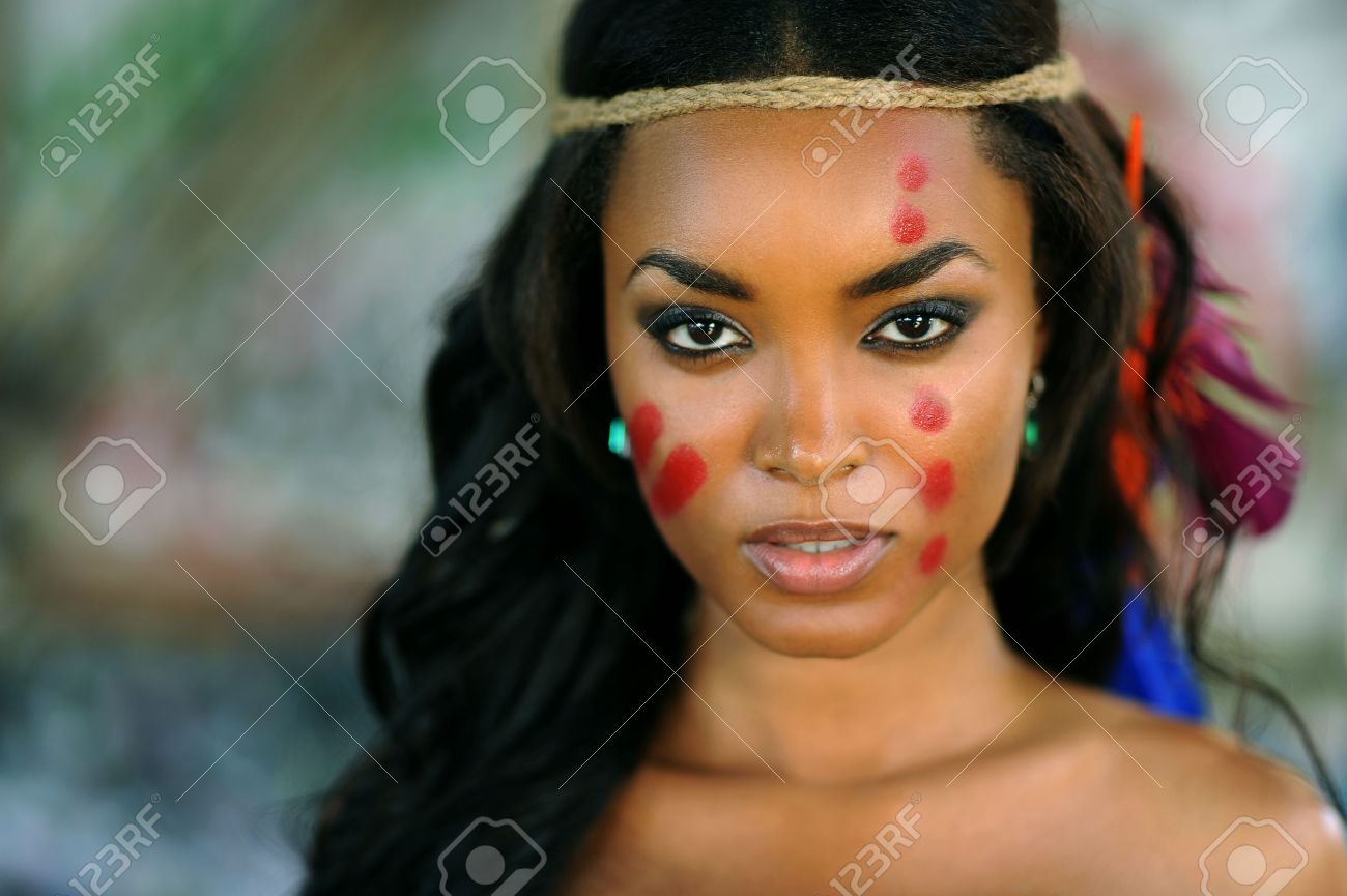 portrait der jungen schonen indischen cherokee frau mit federn im haar und traditionellen make up auf abstrakte hintergrund