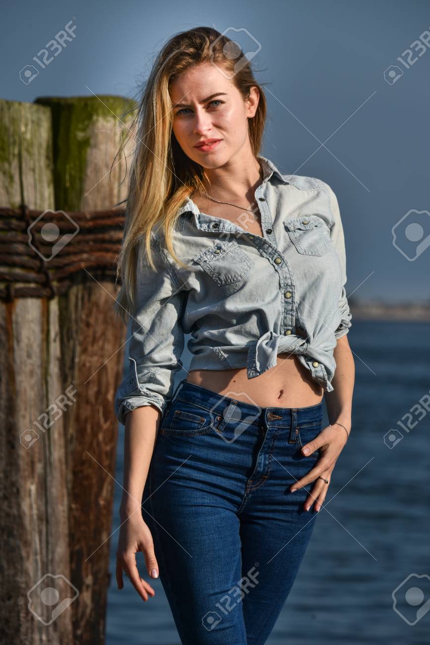 ファッション デニム シャツとジーンズを背景に水とマリーナの船でポーズを身に着けている金髪の女の子 の写真素材 画像素材 Image