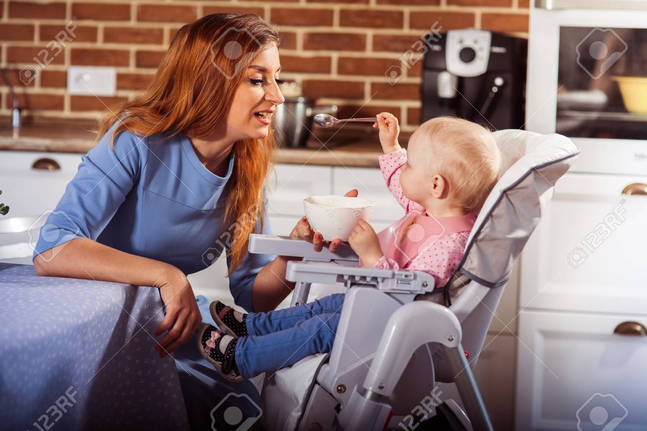little baby girl sits in high chair and feeding with spoon her