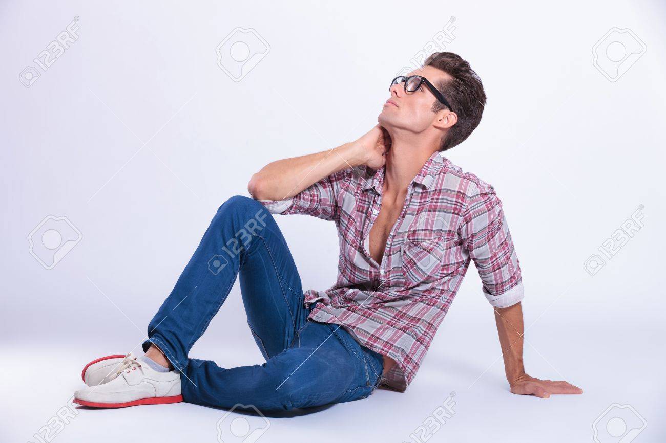 Joven Casual Posando En El Suelo Con Su Mano En Su Cuello Y Mirando Hacia Arriba Lejos De La Camara Sobre Fondo Gris Fotos Retratos Imagenes Y Fotografia De Archivo Libres De