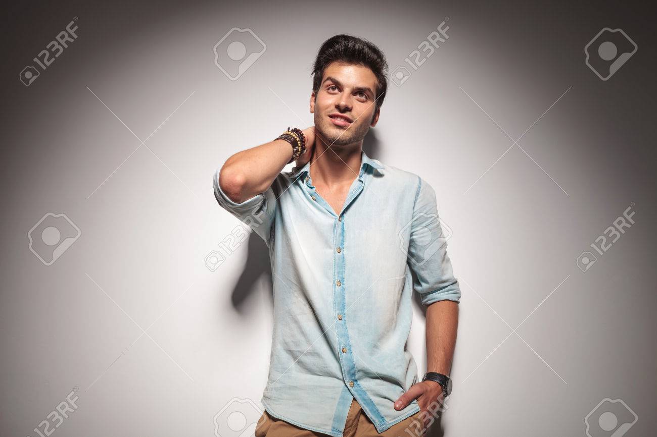 Atractivo Hombre De Moda Joven Apoyado En Una Pared Gris Mientras Mantiene Su Mano Detras De Su Cuello Mirando Hacia Arriba Fotos Retratos Imagenes Y Fotografia De Archivo Libres De Derecho Image