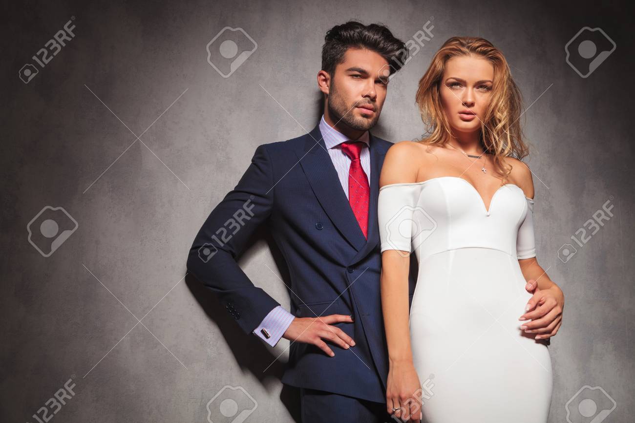 young elegant fashion couple looking away from the camera in studio, while standing with hands on hips, man holding his woman by her waist - 46720285 young elegant fashion couple looking away from the camera in studio, while standing with hands on hips, man holding his woman by her waist - 46720285