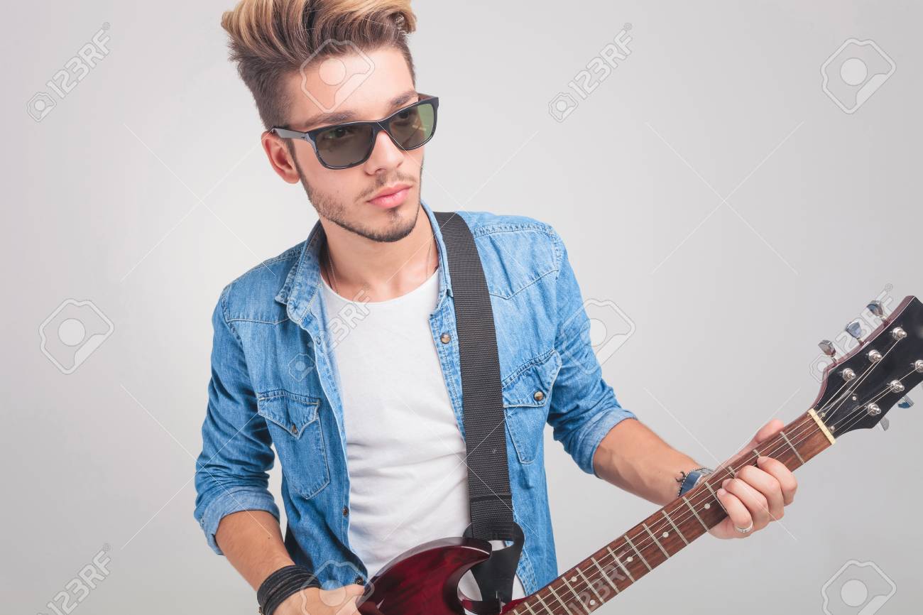 スタジオの背景でよそ見しながらギターを弾く若者のファッションのアーティスト の写真素材 画像素材 Image