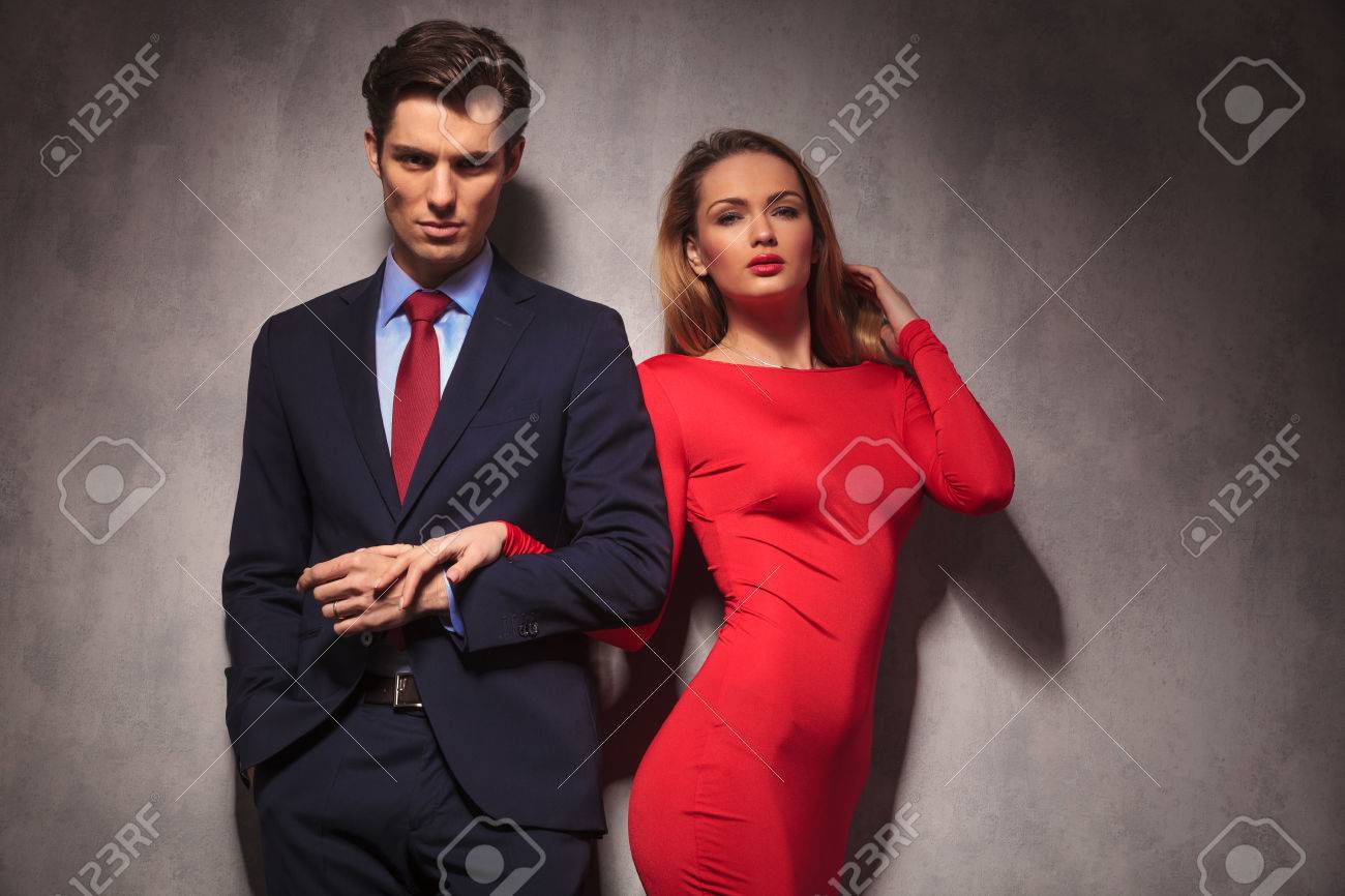 セクシーなエレガントなカップルはスーツとネクタイ 赤いドレスを着た女性に男の手を握っています の写真素材 画像素材 Image