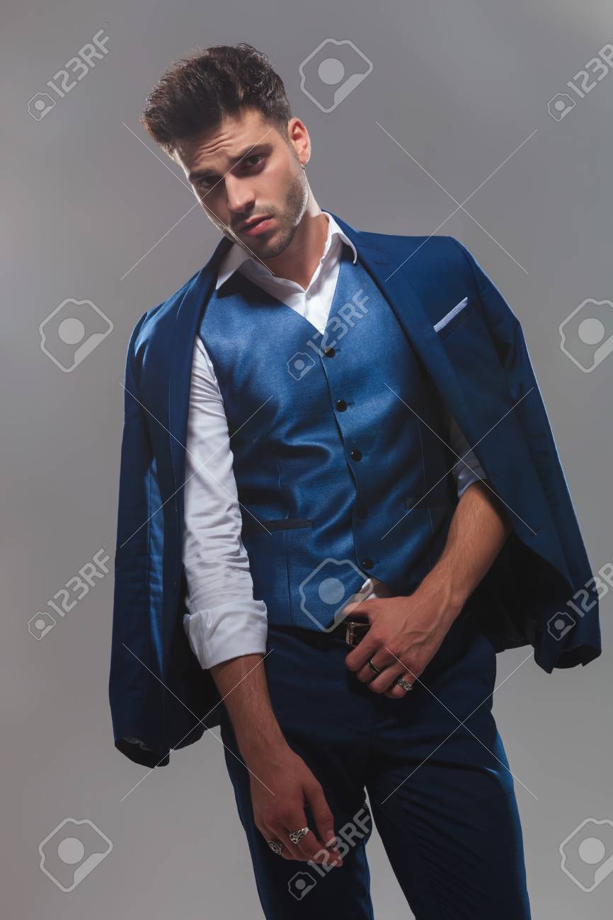 portrait of classy man wearing a blue suit holding belt while..