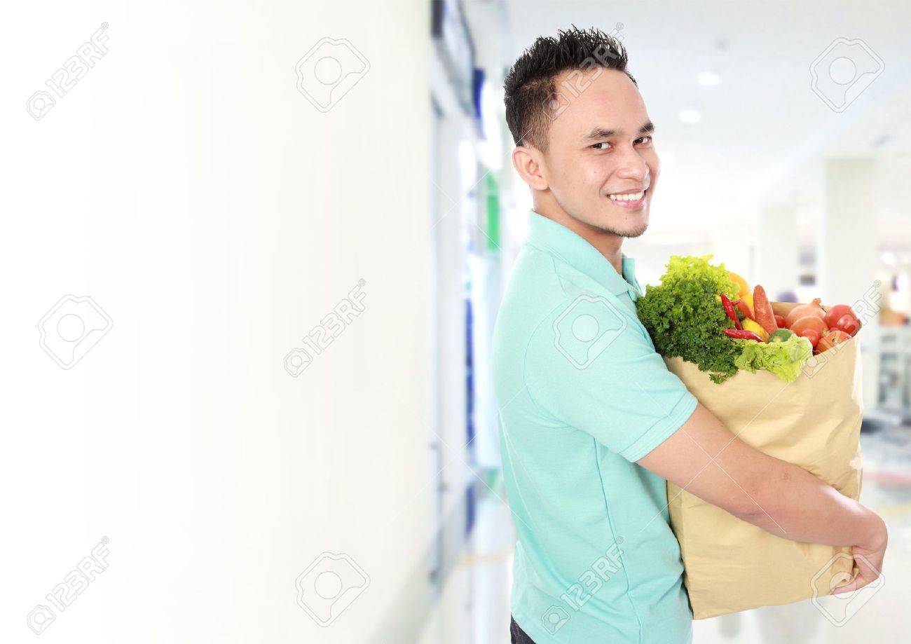 Retrato de la bolsa de comestibles sonriente joven hombre celebración llena de comestibles en el supermercado Retrato de la bolsa de comestibles sonriente joven hombre celebración llena de comestibles en el supermercado