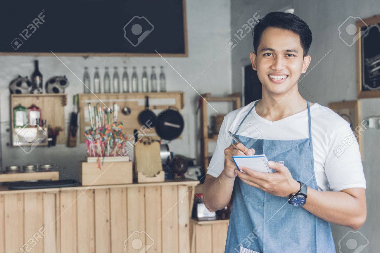 Happy asian male waiter in apron writing order and looking at camera - 55560095 Happy asian male waiter in apron writing order and looking at camera - 55560095