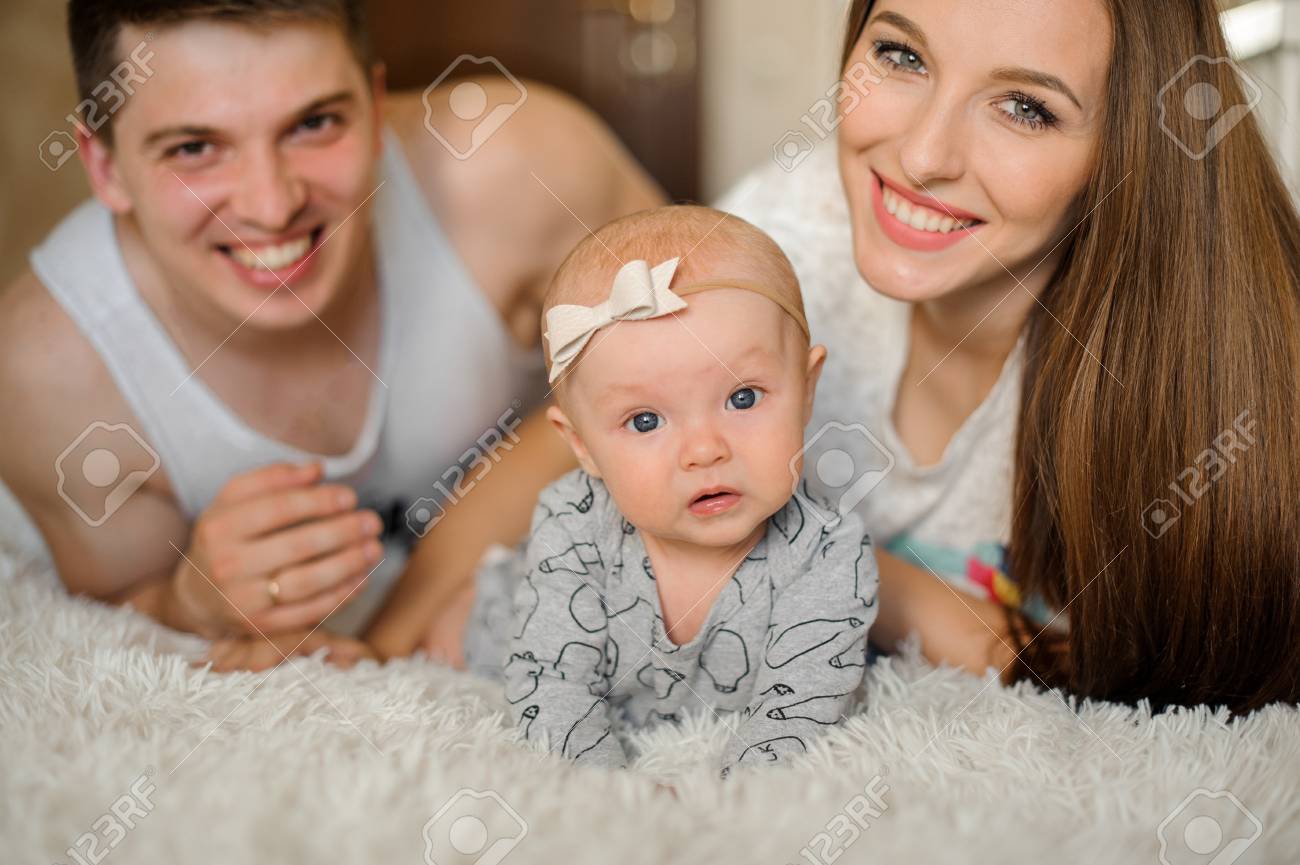 Happy And Young Smiling Parents Couple Lying On The Bed With