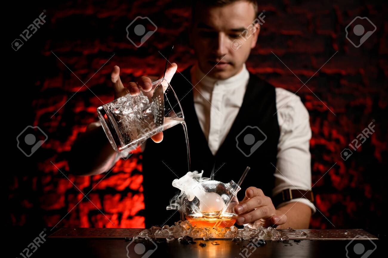 Man barman professionally pours cold drink into smoky designer flask - 145022579 Man barman professionally pours cold drink into smoky designer flask - 145022579