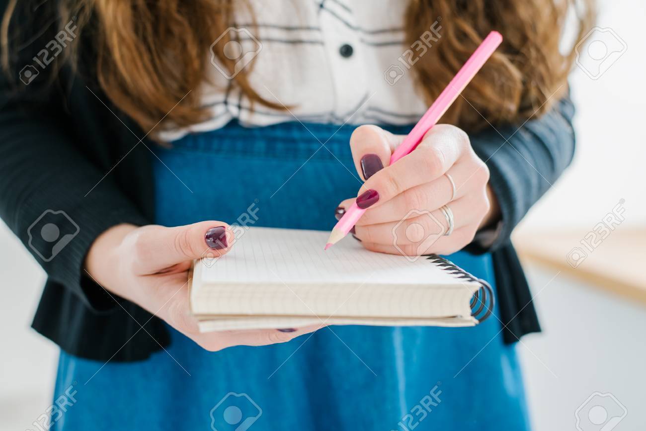 Woman's hand using a pink pencil noting on notepad - 42327526 Woman's hand using a pink pencil noting on notepad - 42327526