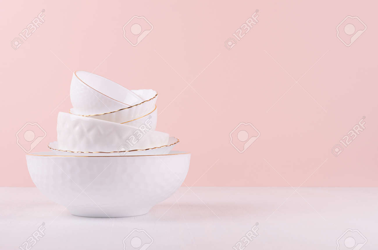 White ceramic crockery stack with golden bezel, different texture on white wooden table, soft light pastel pink wall, elegant delicate kitchen interior. - 168468815 White ceramic crockery stack with golden bezel, different texture on white wooden table, soft light pastel pink wall, elegant delicate kitchen interior. - 168468815