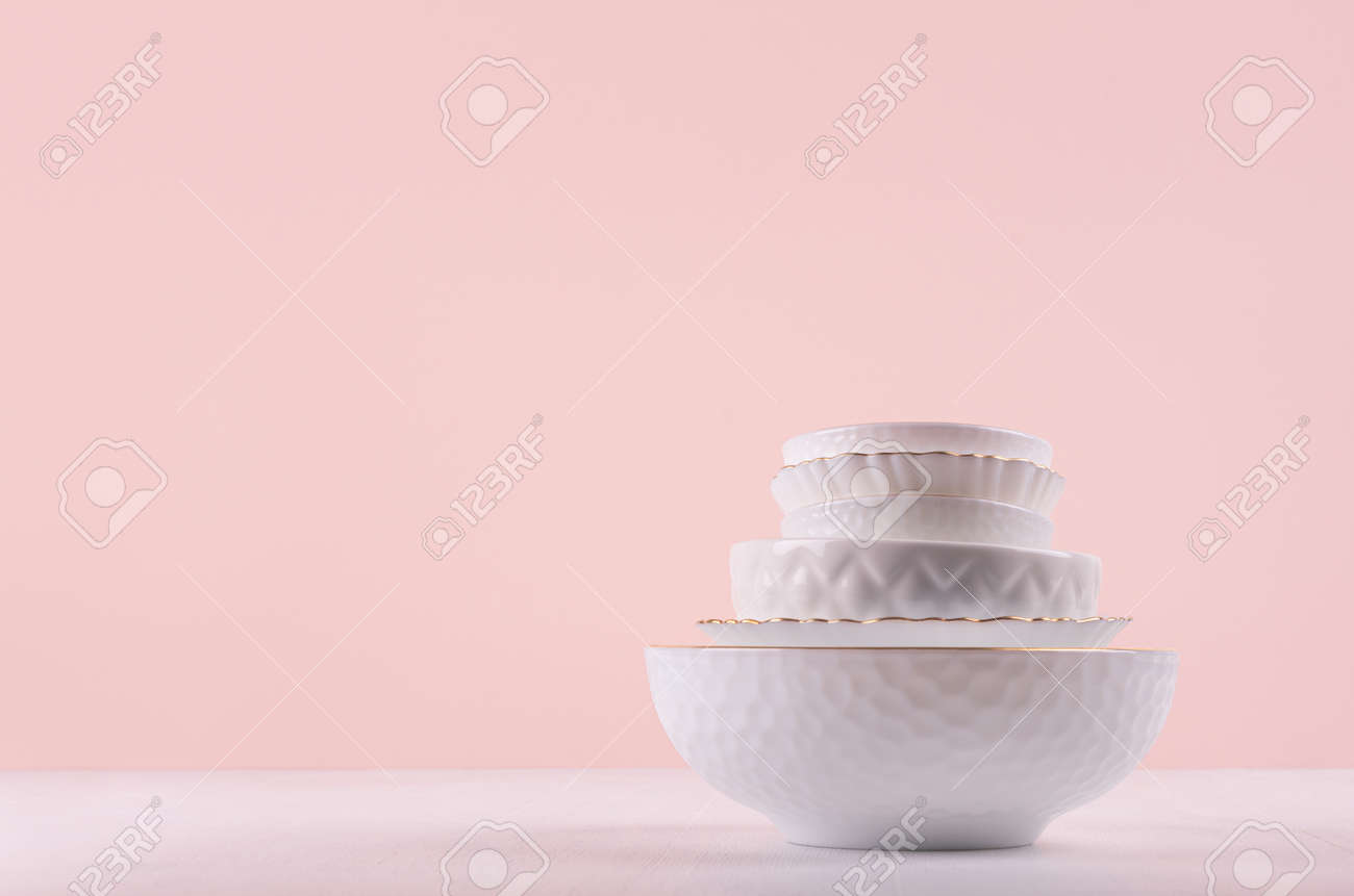 White ceramic dishes with thin gold border, different tracery form on white wood table in delicate pastel pink interior. - 168468866 White ceramic dishes with thin gold border, different tracery form on white wood table in delicate pastel pink interior. - 168468866