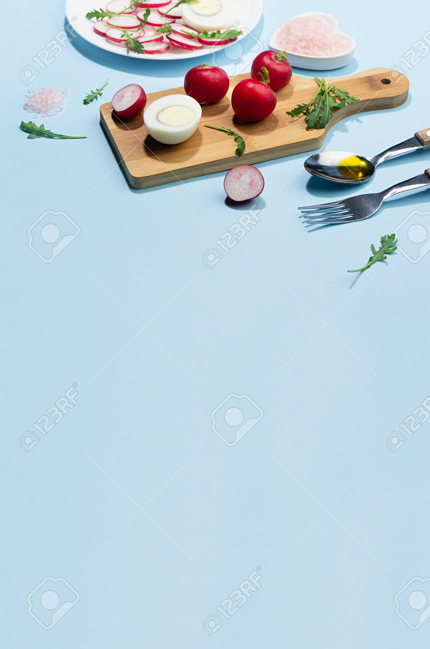 Dieting salad of fresh vegetables - radish, arugula and eggs with shadow in hard light on blue background and white wood table, border, vertical. - 168468895 Dieting salad of fresh vegetables - radish, arugula and eggs with shadow in hard light on blue background and white wood table, border, vertical. - 168468895