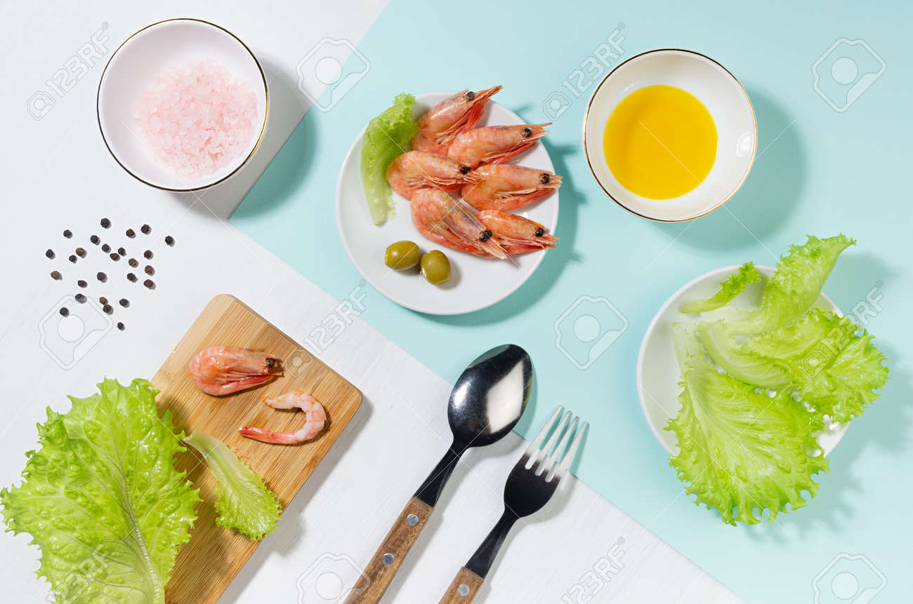 Healthy lifestyle - cooking of fresh salad of prawn, green salad, olive, black pepper, pink salt in sunlight with shadow, flat lay, on white wooden table, minty background. - 168468909 Healthy lifestyle - cooking of fresh salad of prawn, green salad, olive, black pepper, pink salt in sunlight with shadow, flat lay, on white wooden table, minty background. - 168468909