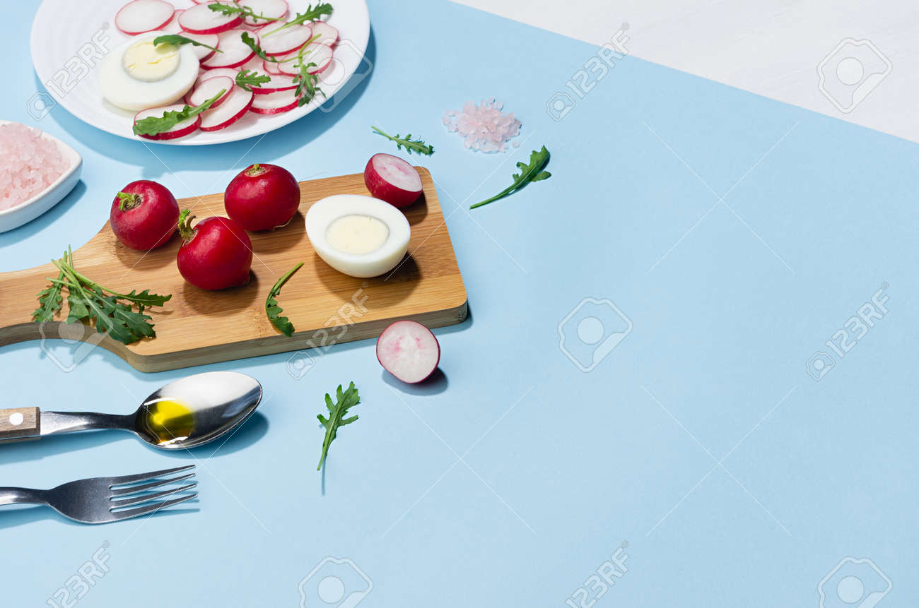 Dieting salad of fresh vegetables - radish, arugula and eggs with shadow in hard light on blue background and white wood table, border. - 168468915 Dieting salad of fresh vegetables - radish, arugula and eggs with shadow in hard light on blue background and white wood table, border. - 168468915