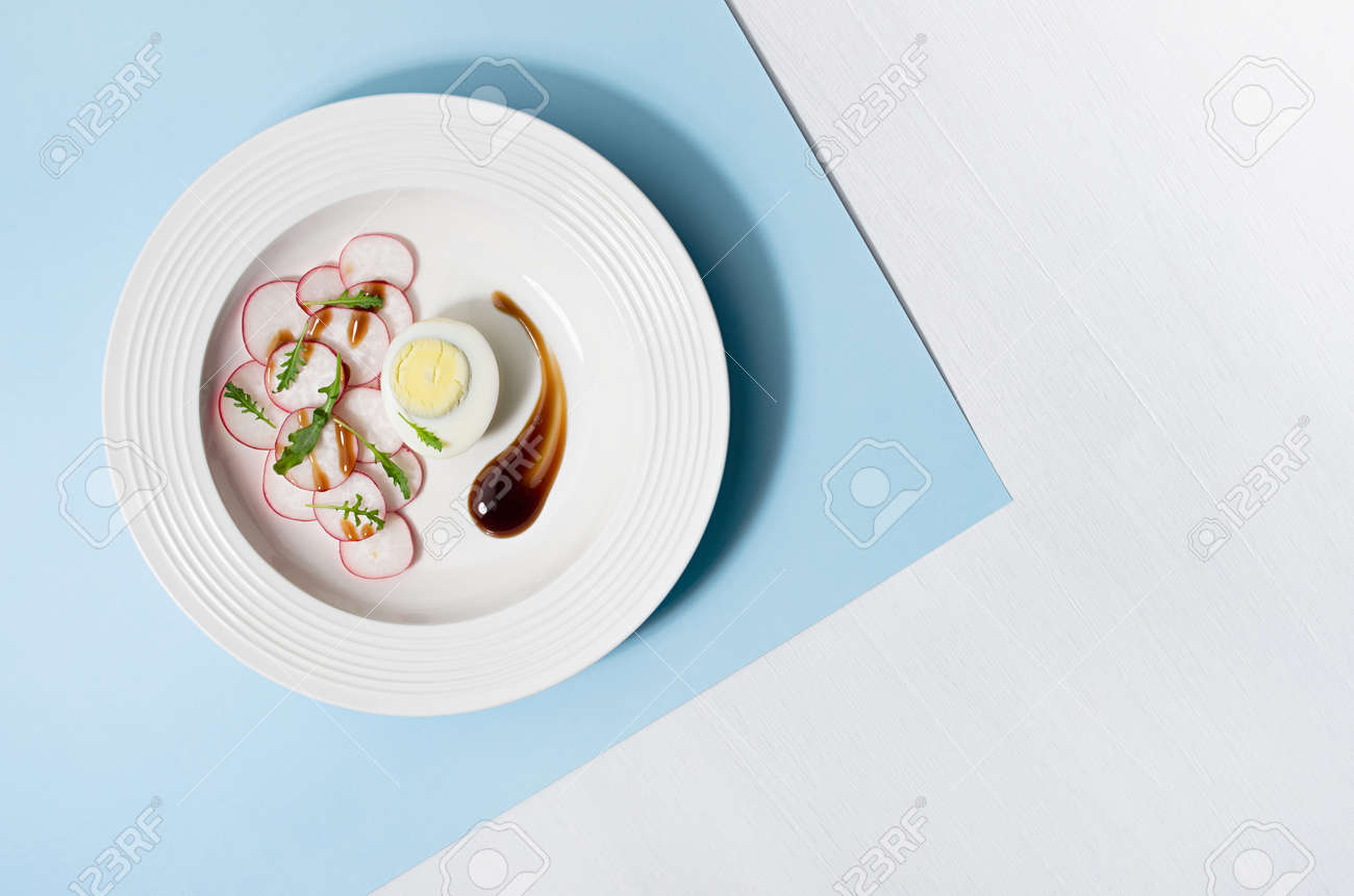 Spring vegetable salad of radish, arugula and eggs with balsamic sauce in white plate on pastel blue background with shadow in hard light, top view. - 168468922 Spring vegetable salad of radish, arugula and eggs with balsamic sauce in white plate on pastel blue background with shadow in hard light, top view. - 168468922