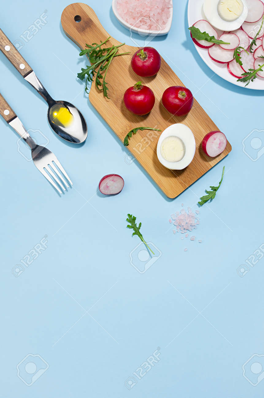 Healthy lifestyle - cooking of spring salad of raw fresh vegetables - radish, arugula with eggs in sunlight with shadow, top view, vertical, on white wooden table, blue background. - 168468924 Healthy lifestyle - cooking of spring salad of raw fresh vegetables - radish, arugula with eggs in sunlight with shadow, top view, vertical, on white wooden table, blue background. - 168468924