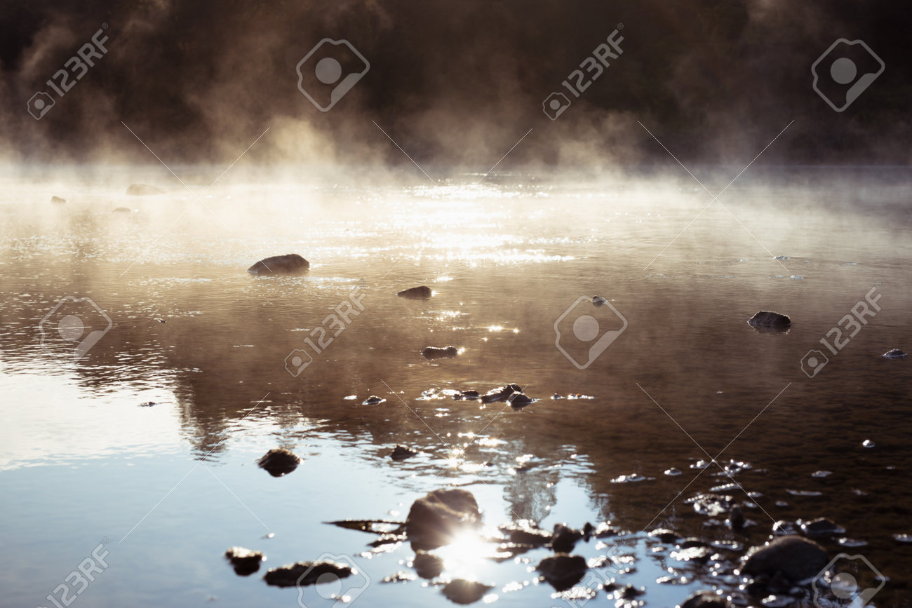 이른 아침 강물 위에 푹신한 하얀 안개가 황금빛 햇빛에 반사되어 물에 반사되는 잔물결과 해안의 밝고 차분한 자연 배경에 실루엣 검은  돌이 있습니다. 로열티 무료 사진, 그림, 이미지 그리고 스톡포토그래피. Image 199996184