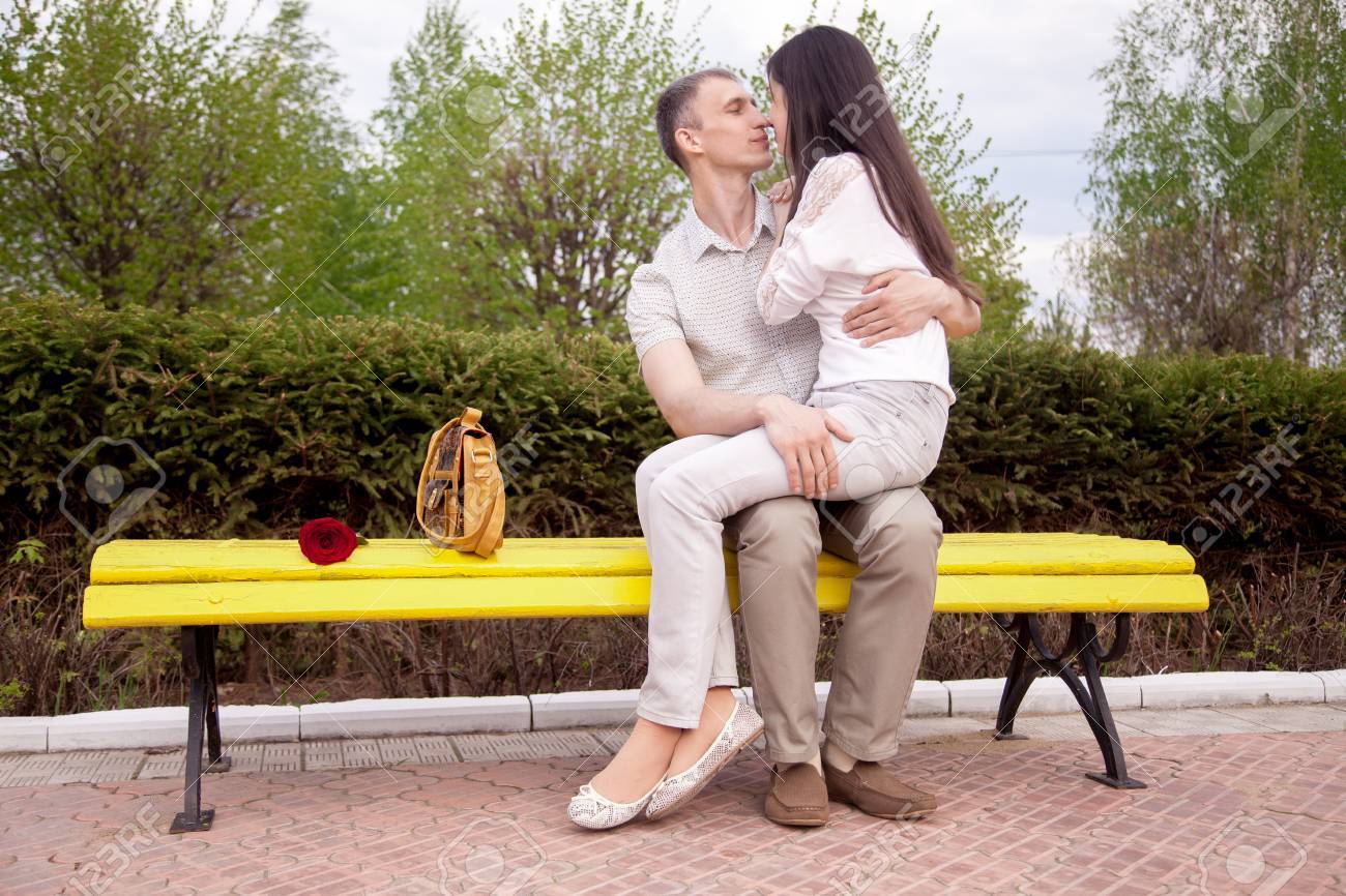 赤いバラ公園で黄色のベンチにキスを彼女の彼氏の周は フルの長さの上に座っている若い女性とカップルの肖像画 の写真素材 画像素材 Image