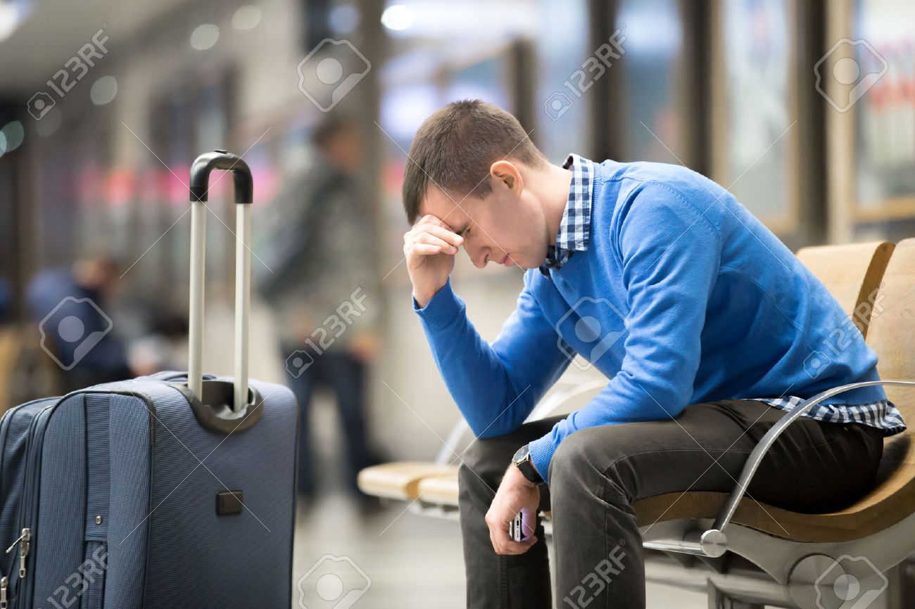 Portrait of young handsome guy wearing casual style clothes waiting for transport. Tired traveler man travelling with suitcase sitting with frustrated facial expression on a chair in modern station - 54552648 Portrait of young handsome guy wearing casual style clothes waiting for transport. Tired traveler man travelling with suitcase sitting with frustrated facial expression on a chair in modern station - 54552648