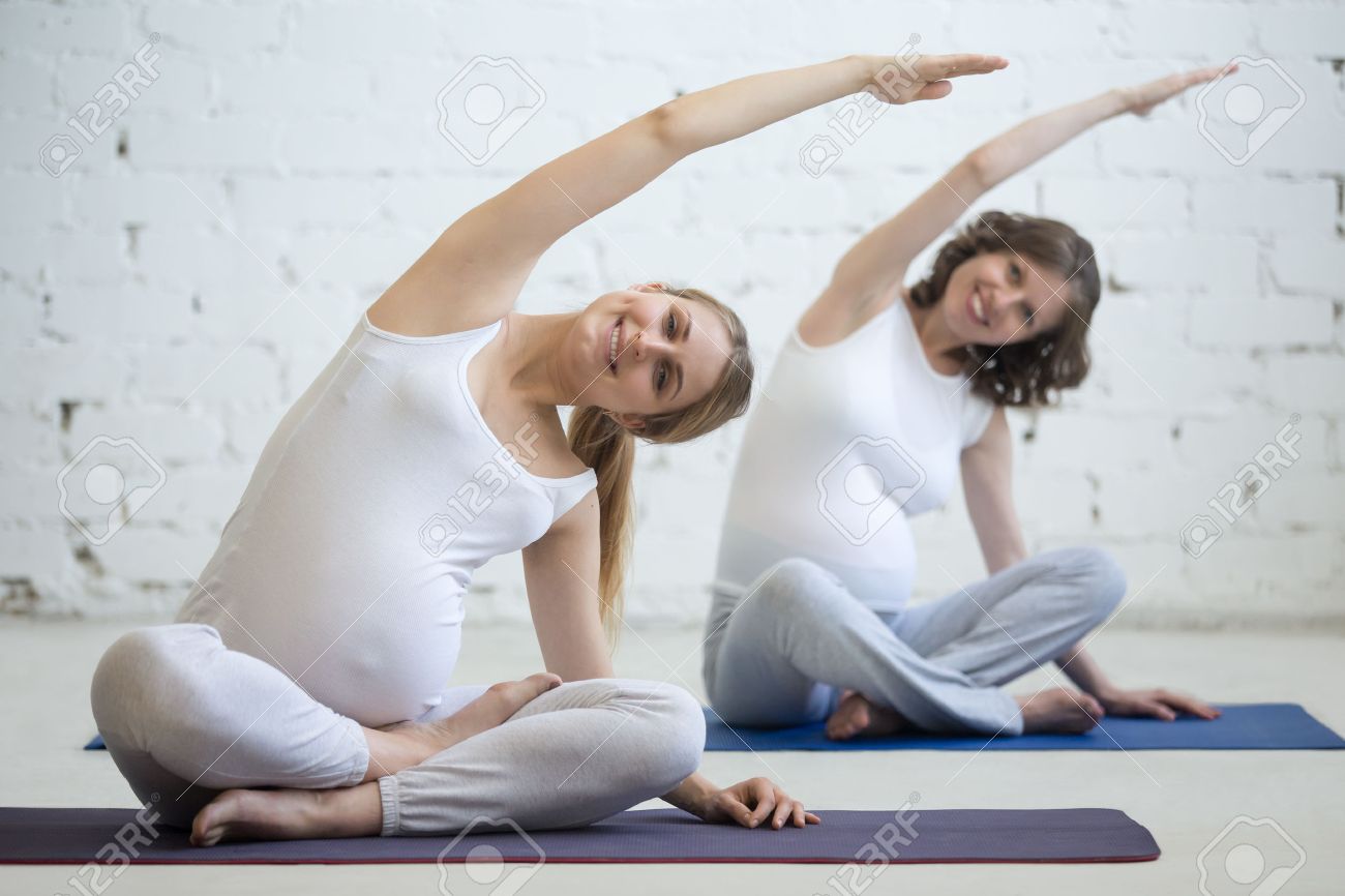 妊娠中のヨガ フィットネスの概念 屋内作業を 2 つの美しい若い妊婦ヨガ モデル 妊娠中笑みを浮かべてフィットネスの女性クラスでヨガのあぐらポーズ で座っています 簡単なポーズで出生前 Sidebend の写真素材 画像素材 Image