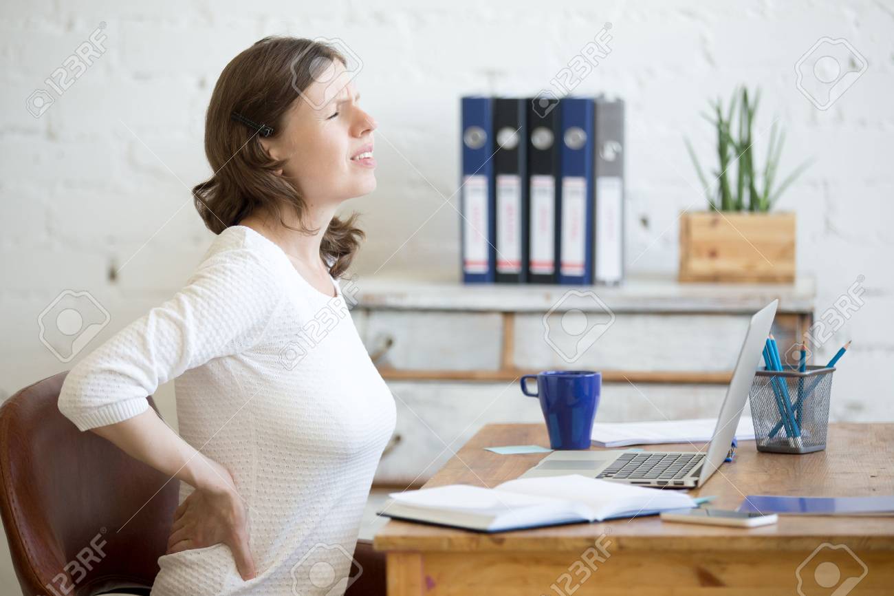 Young stressed businesswoman sitting in front of laptop and holding her waist with pained expression. Business woman feeling pain, touching aching back, suffering from backache after working on pc - 62328995 Young stressed businesswoman sitting in front of laptop and holding her waist with pained expression. Business woman feeling pain, touching aching back, suffering from backache after working on pc - 62328995