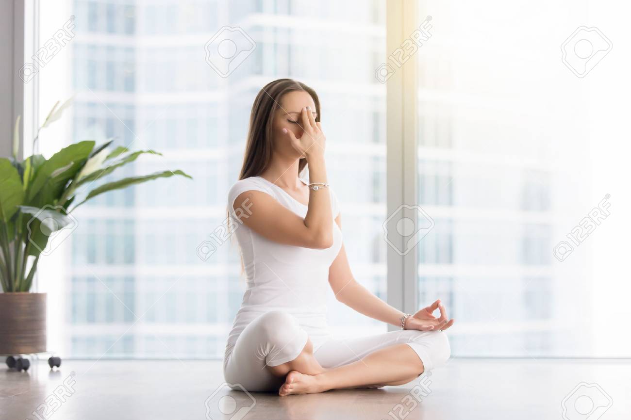 ヨガの練習 Sukhasana ポーズ 代替の鼻孔の呼吸法 ナンディ Shodhana プラナヤマに座って ワークアウト 白スポーツウェア 屋内完全な長さを身に着けている若い女性 の写真素材 画像素材 Image