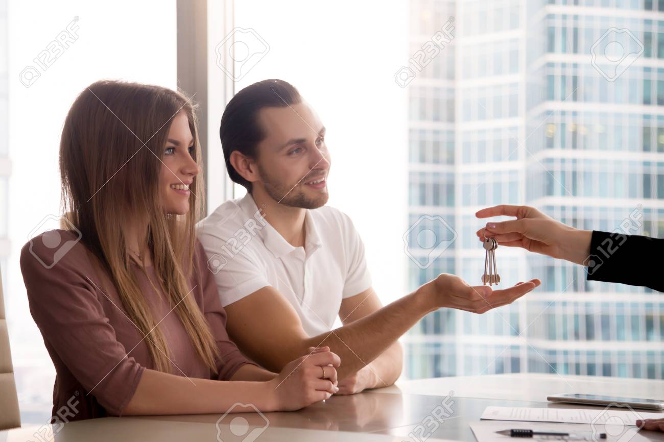 A Hand Of Female Real Estate Agent Giving Keys To Own First Apartment Couple A Hand Of Female Real Estate Agent Giving Keys To Own First Apartment Couple