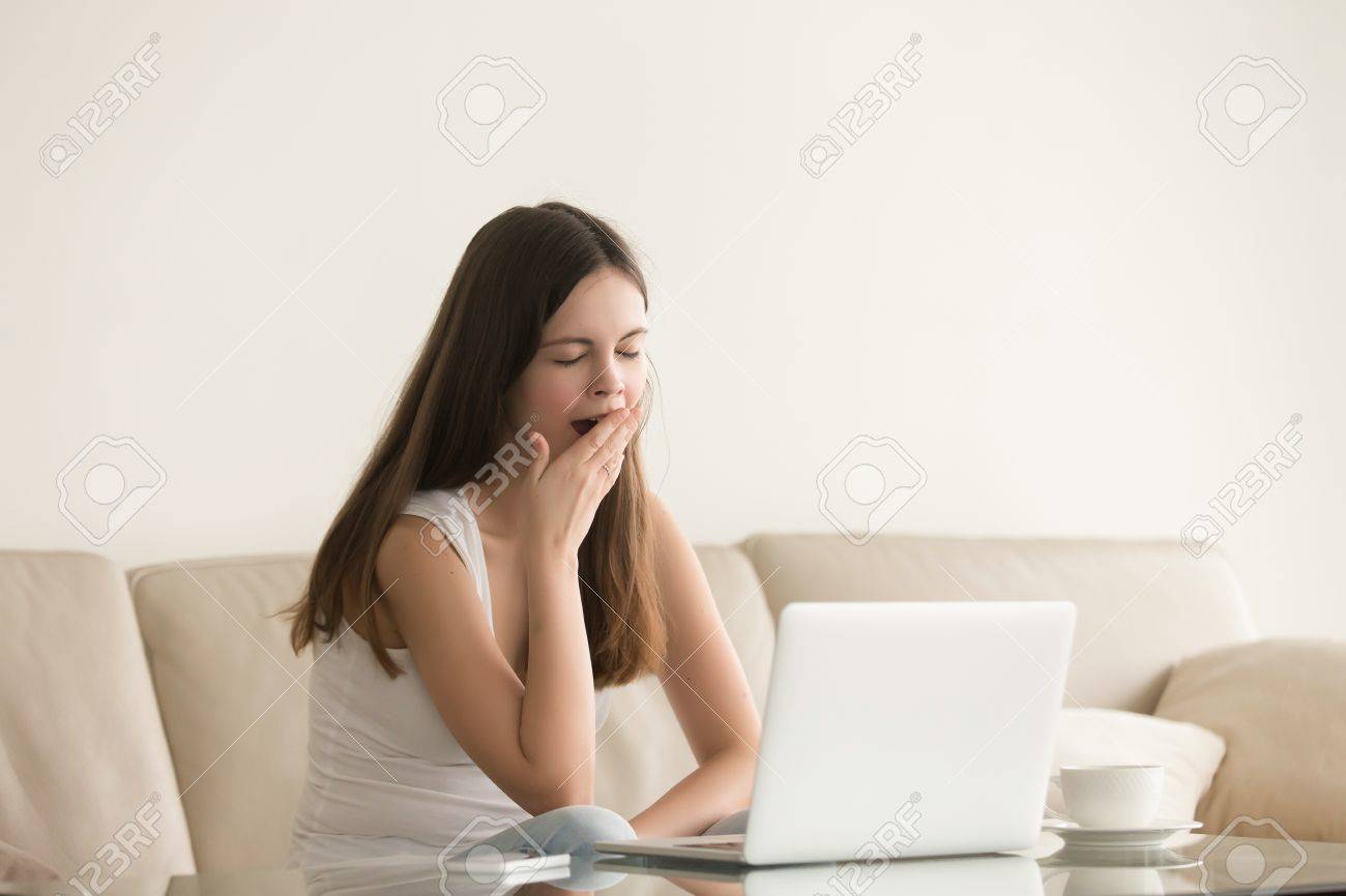 若い女性は ノート パソコンの前のソファに座ってあくび コンピューターのすべての夜を働いて疲れてかなり女性フリーランサー 学生は勉強の長い時間後睡眠と眠気の欠如を感じています の写真素材 画像素材 Image