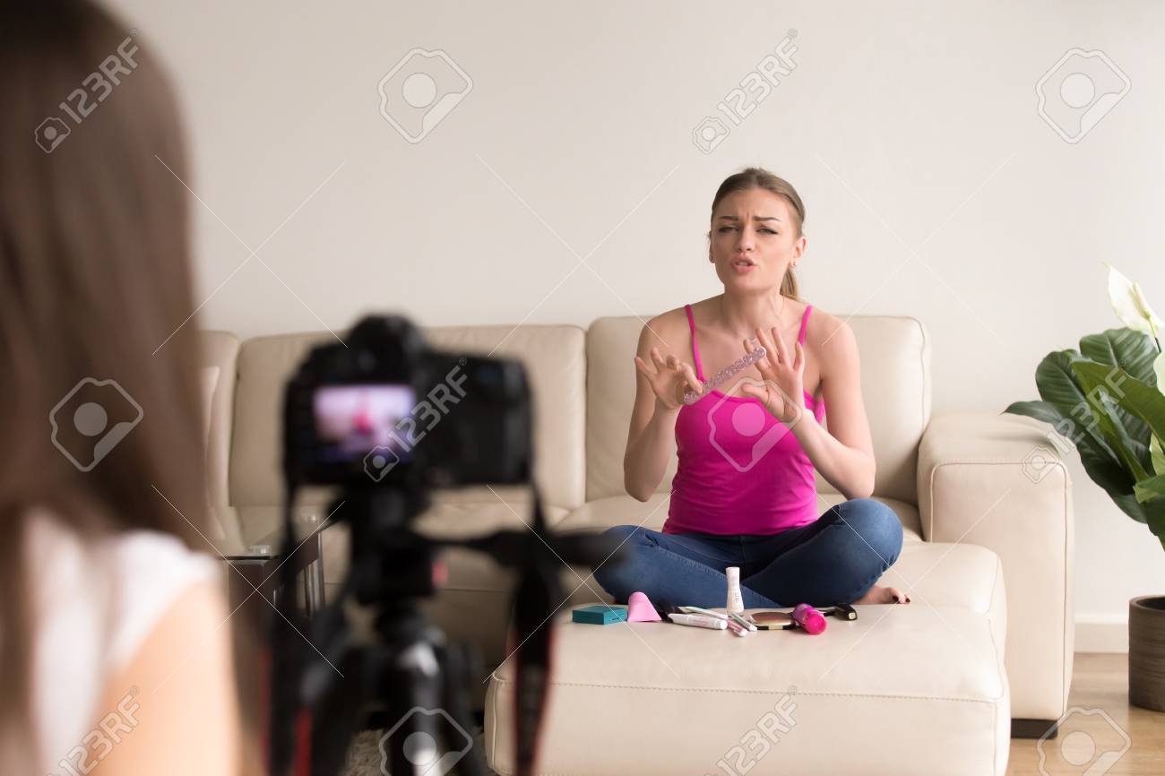 ビデオカメラの前に爪のバッファーを使用して魅力的な若い女性のソファーに座っていると マニキュアを作る2 つのガール フレンドが ストリーミング オンライン ワーク ショップ さまざまな化粧品の製品 美容ビデオブログを記録 の写真素材 画像素材 Image