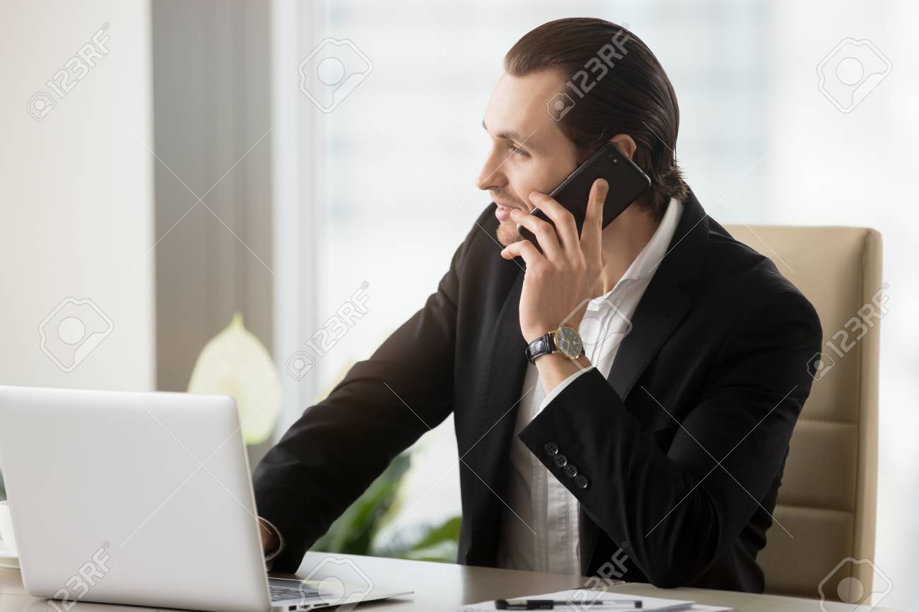 携帯電話で話すラップトップの前のワークデスクで現代のオフィスで笑顔の若いビジネスマン 取引の話し合い 将来の会議の計画 商談 クライアントコンサルティングのコンセプトを成功に与えます の写真素材 画像素材 Image 85638357