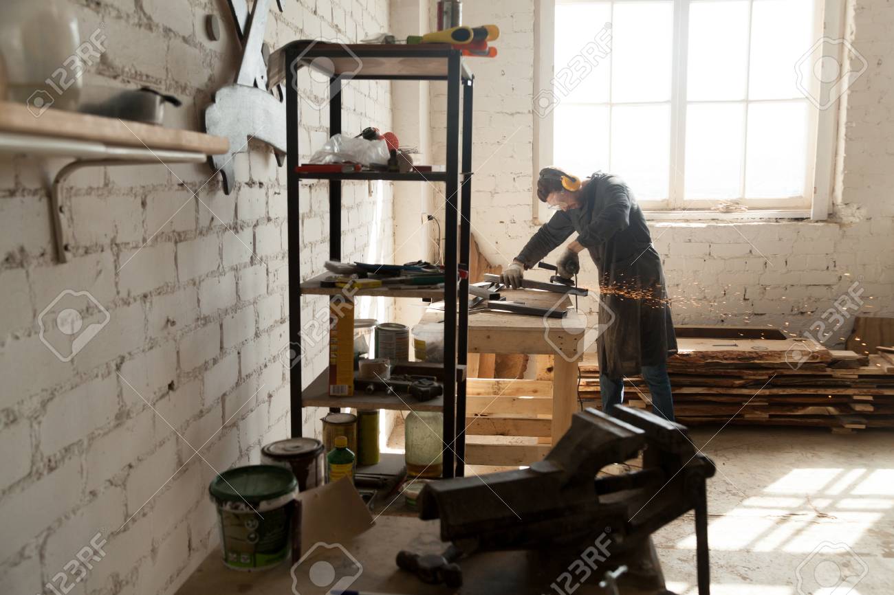 Skilled Cabinet Maker Working With Angle Grinder In Small Workshop
