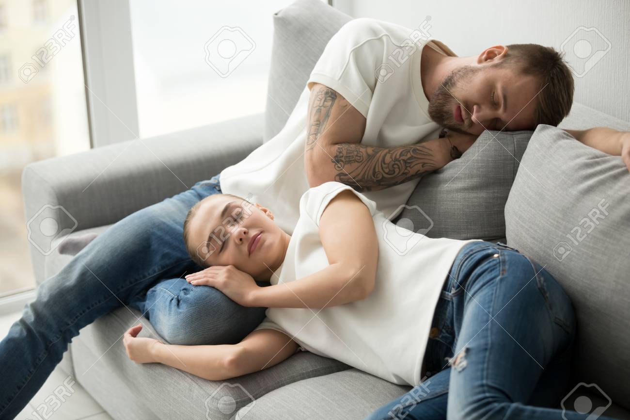 一緒に快適なソファで眠っているリラックスした若いカップル 柔らかいソファで昼間に快適な昼寝をして眠っている疲れた怠惰な男女 居心地の良いリビングルームで自宅でくつろぐ の写真素材 画像素材 Image