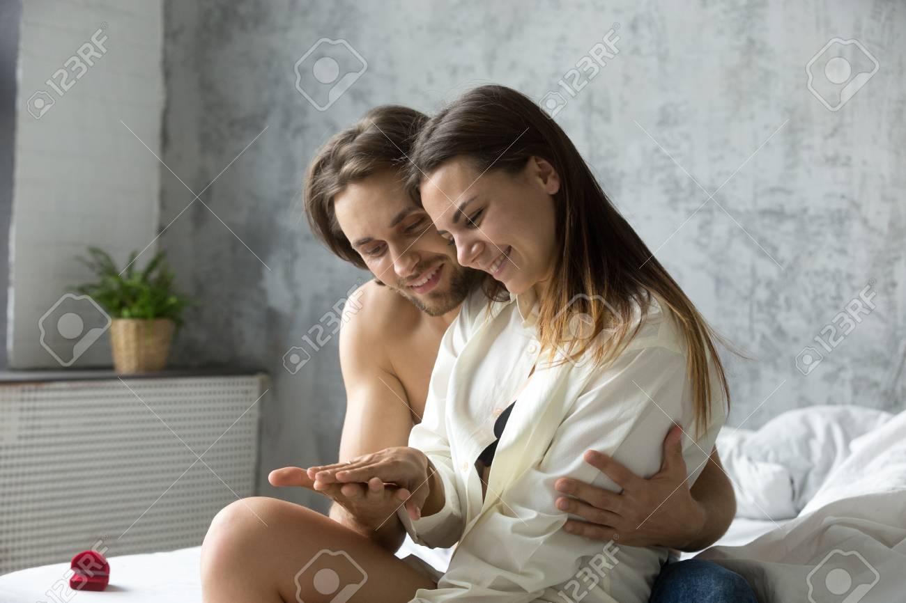 사랑에 빠진 젊은 커플은 함께 침실에 앉아 미래를 생각하면서 제안 후 순간을 즐기며 행복한 여자친구는 남자친구와 결혼하기로 동의하며  결혼반지를 손가락에 얹는다 로열티 무료 사진, 그림, 이미지 그리고 스톡포토그래피. Image 99707435