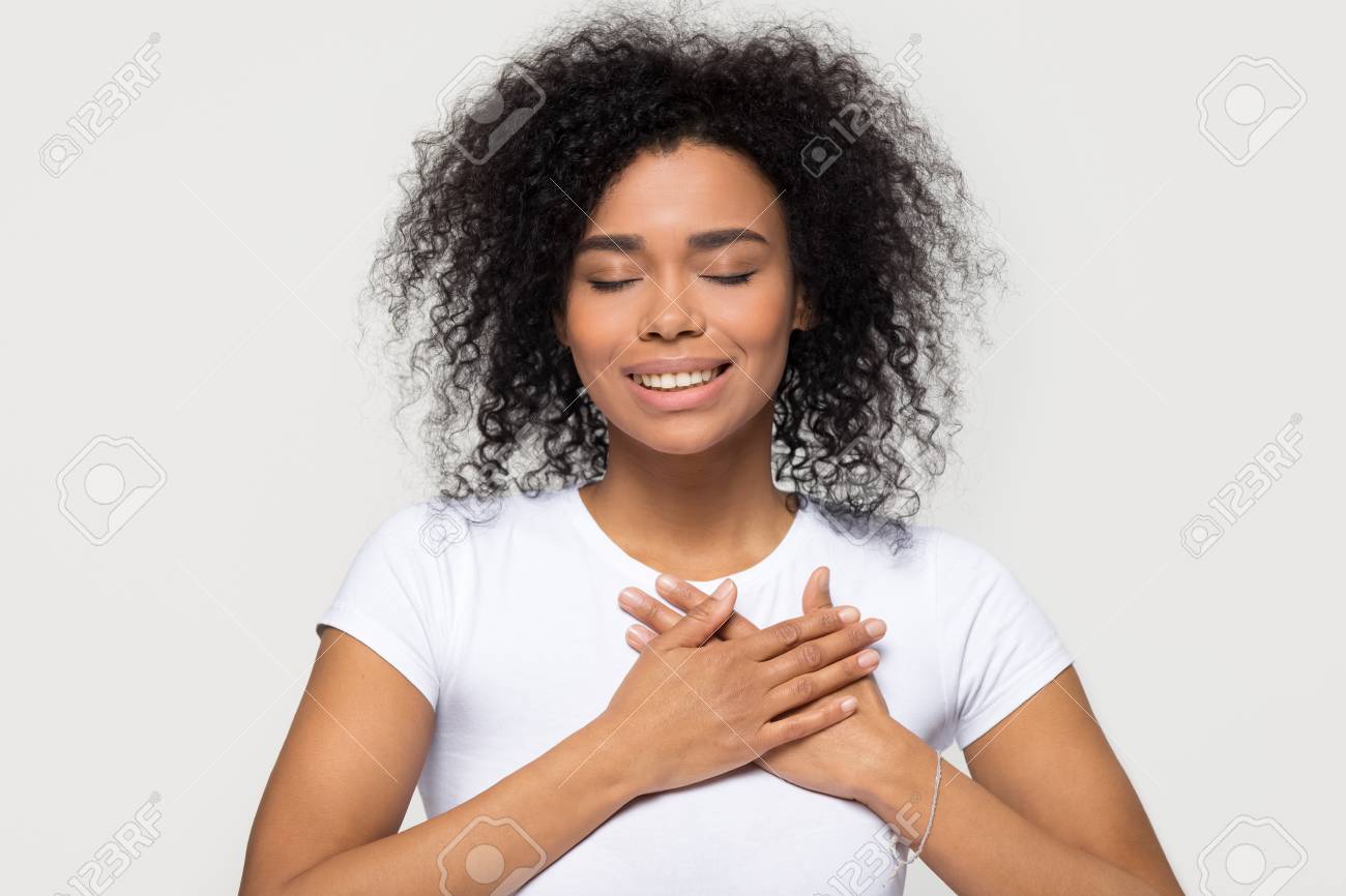 Grateful hopeful happy black woman holding hands on chest feeling pleased thankful, sincere african lady expressing heartfelt love appreciation gratitude honesty isolated on white studio background - 116423100 Grateful hopeful happy black woman holding hands on chest feeling pleased thankful, sincere african lady expressing heartfelt love appreciation gratitude honesty isolated on white studio background - 116423100