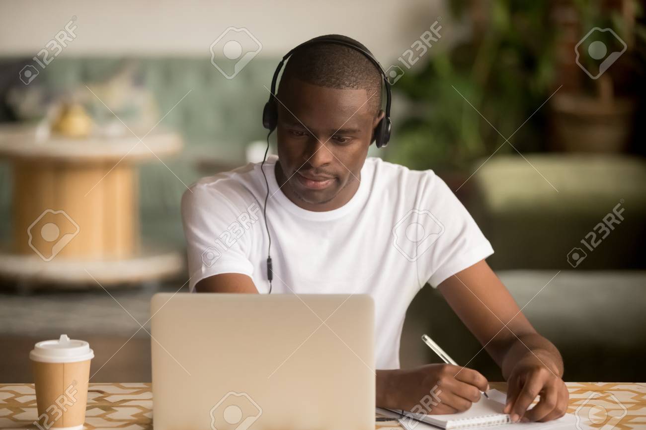 Focused african man wearing headphones watching webinar training making notes study online learning language on computer, black male student looking at laptop elearning in internet write information - 120572362 Focused african man wearing headphones watching webinar training making notes study online learning language on computer, black male student looking at laptop elearning in internet write information - 120572362