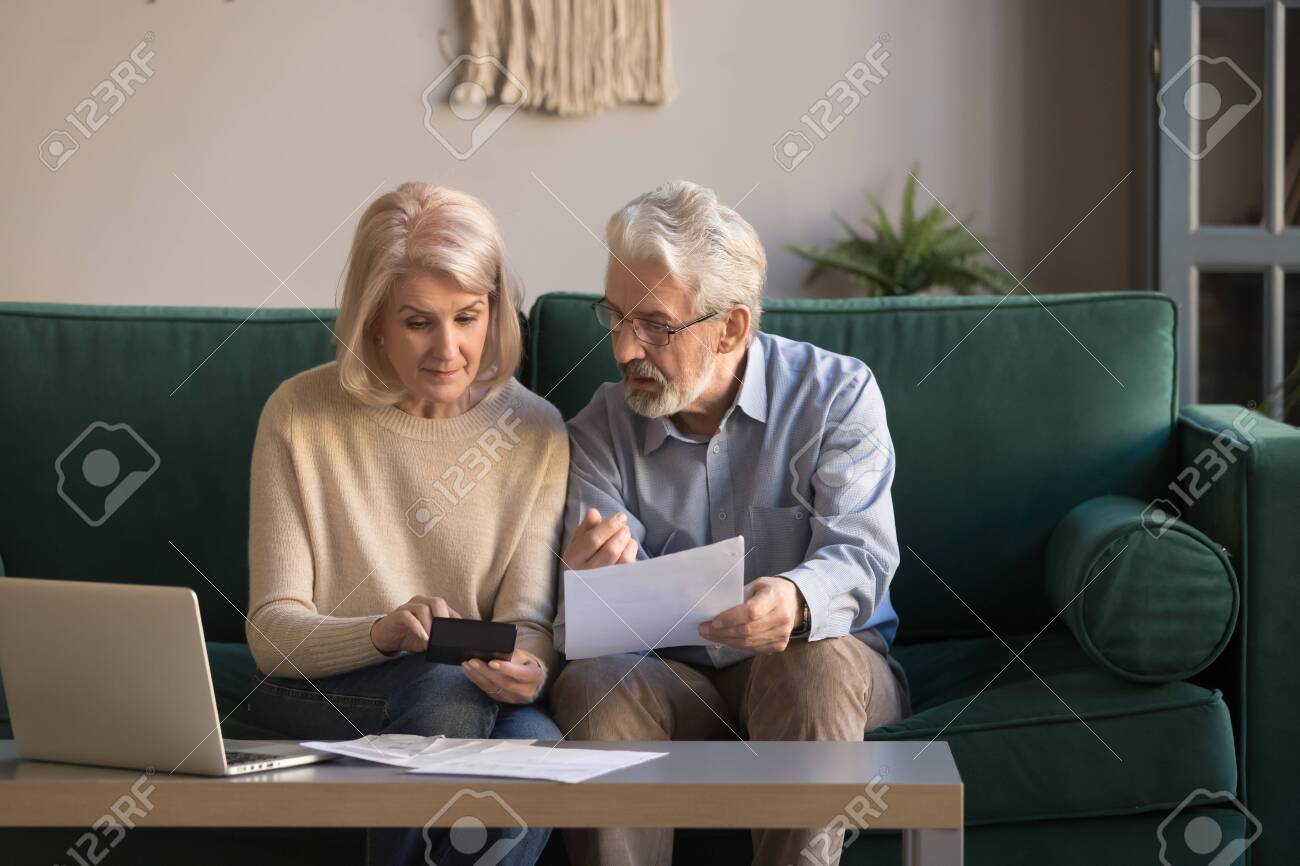 Serious mature couple calculating bills to pay, checking domestic finances, middle aged family managing, planning budget, expenses, grey haired man and woman reading bank loan documents at home - 122246949 Serious mature couple calculating bills to pay, checking domestic finances, middle aged family managing, planning budget, expenses, grey haired man and woman reading bank loan documents at home - 122246949