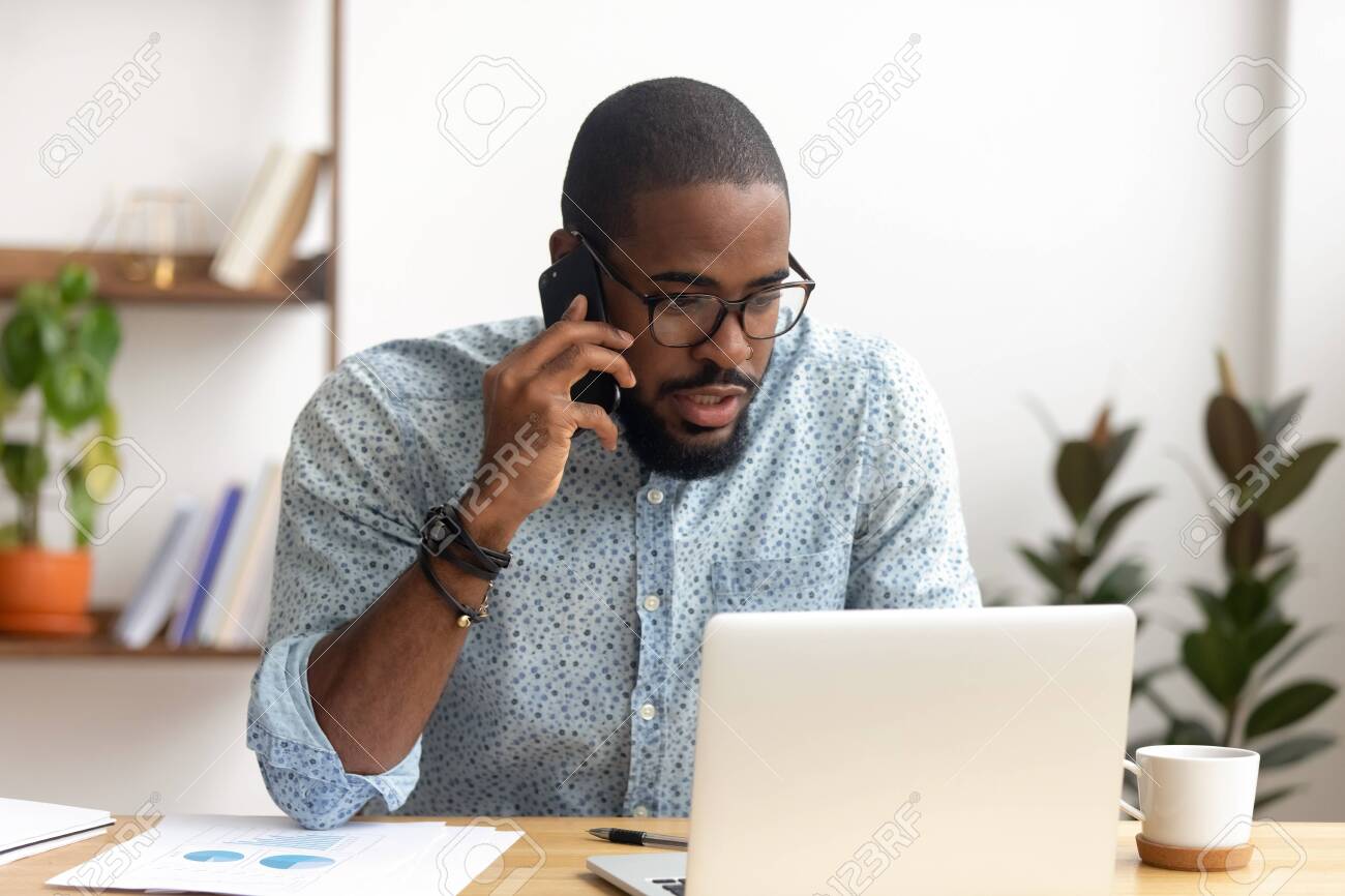 Serious african-american employee making business call focused on laptop at workplace. Black businessman consulting customer, discussing financial report. Contract negotiation and discussion concept - 124259884 Serious african-american employee making business call focused on laptop at workplace. Black businessman consulting customer, discussing financial report. Contract negotiation and discussion concept - 124259884