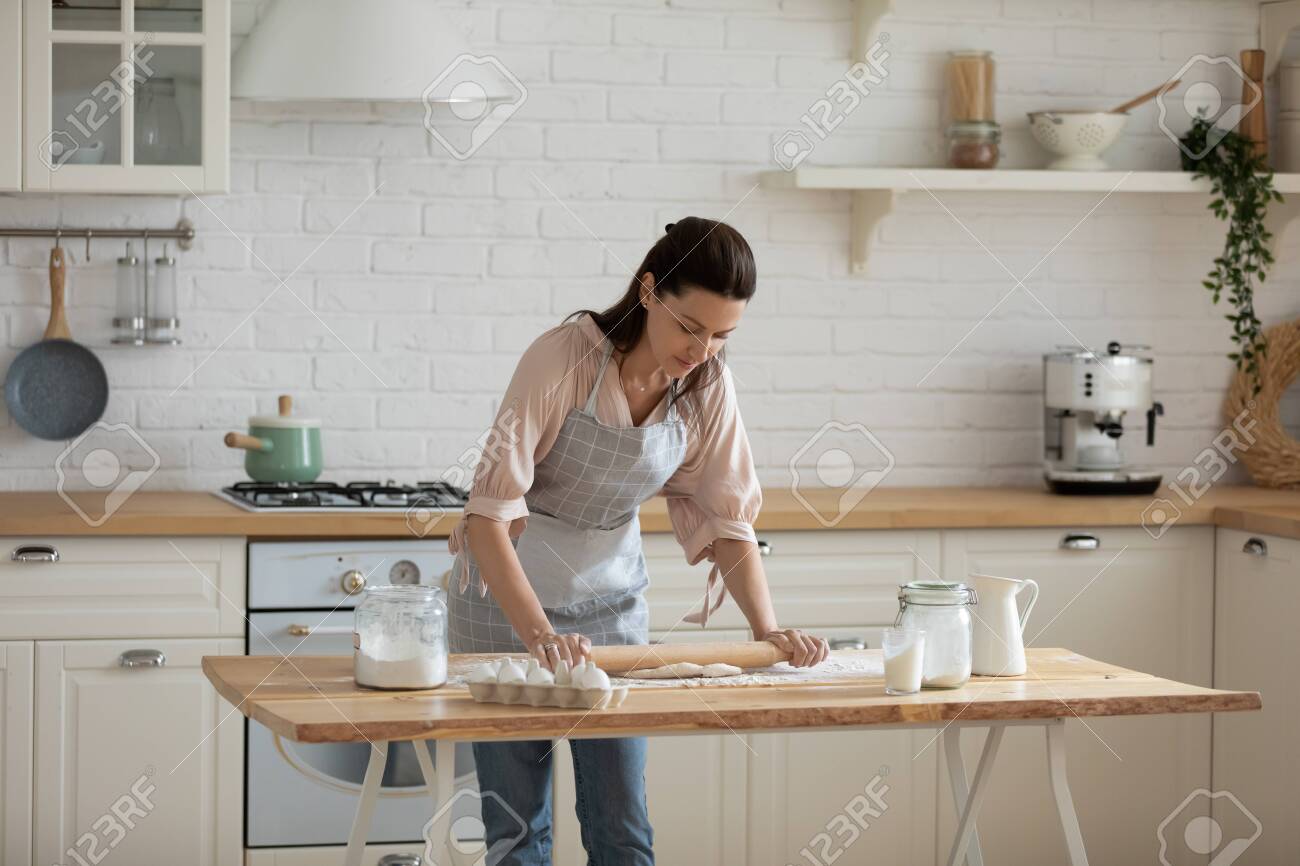 Concentrated busy 30s woman leaning over table, rolling out dough for homemade pastry. Focused pleasant female professional confectioner making clients baking order, preparing food in kitchen at home. - 133969226 Concentrated busy 30s woman leaning over table, rolling out dough for homemade pastry. Focused pleasant female professional confectioner making clients baking order, preparing food in kitchen at home. - 133969226