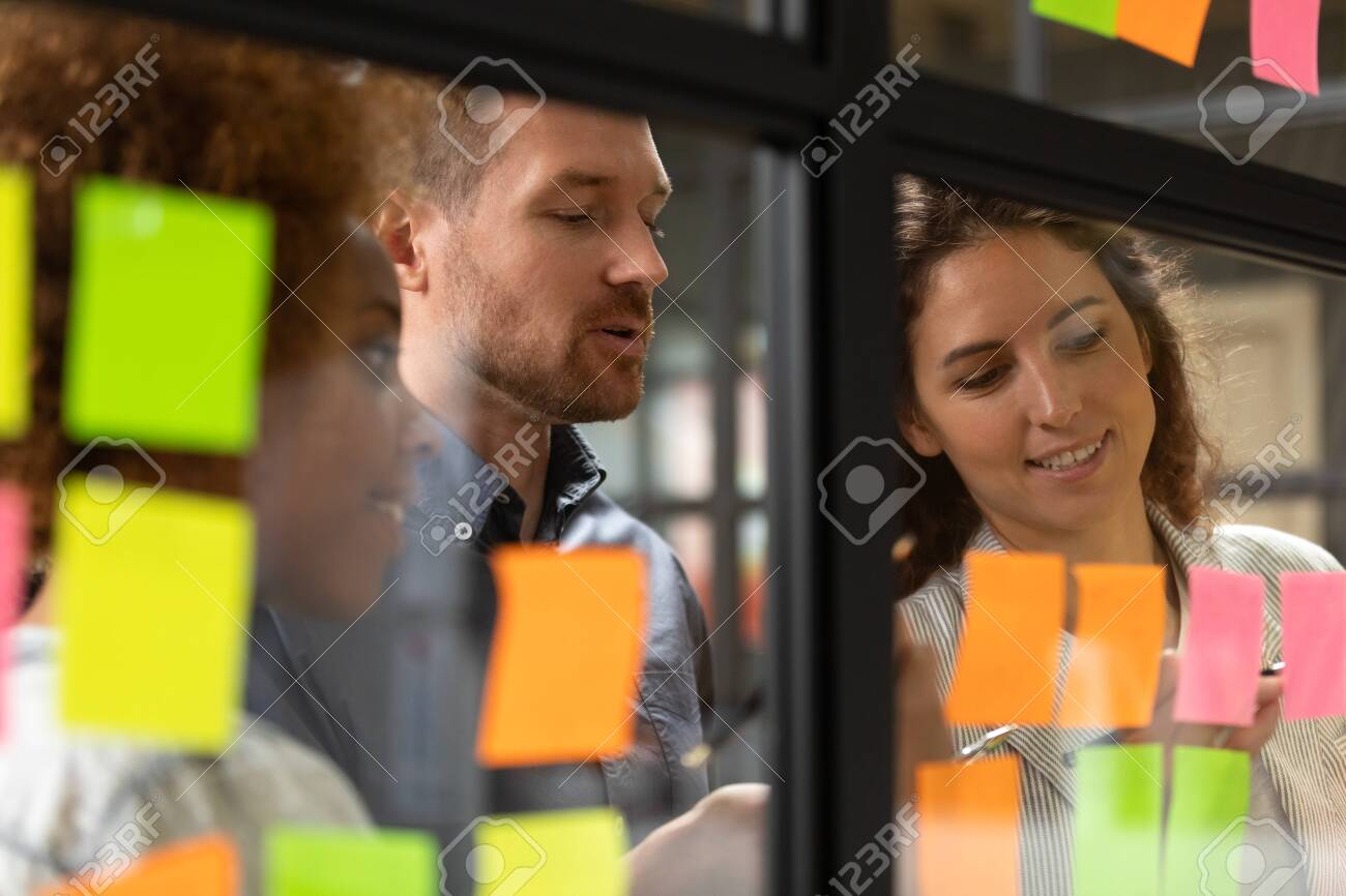 Close up head shot smiling female african american and caucasian colleagues showing working progress to confident male team leader on kanban agile glass window board with colorful paper stickers. - 133969306 Close up head shot smiling female african american and caucasian colleagues showing working progress to confident male team leader on kanban agile glass window board with colorful paper stickers. - 133969306