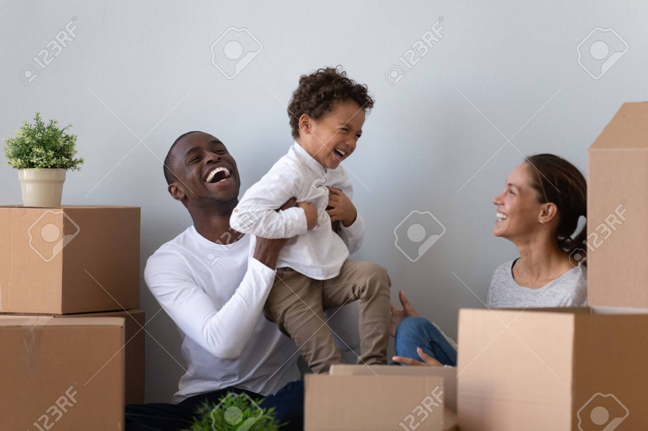 Happy laughing african american young man rising up joyful mixed race cute little son, having fun with wife. Overjoyed smiling multiracial family playing near carton packages, moving in first home. - 134588030 Happy laughing african american young man rising up joyful mixed race cute little son, having fun with wife. Overjoyed smiling multiracial family playing near carton packages, moving in first home. - 134588030