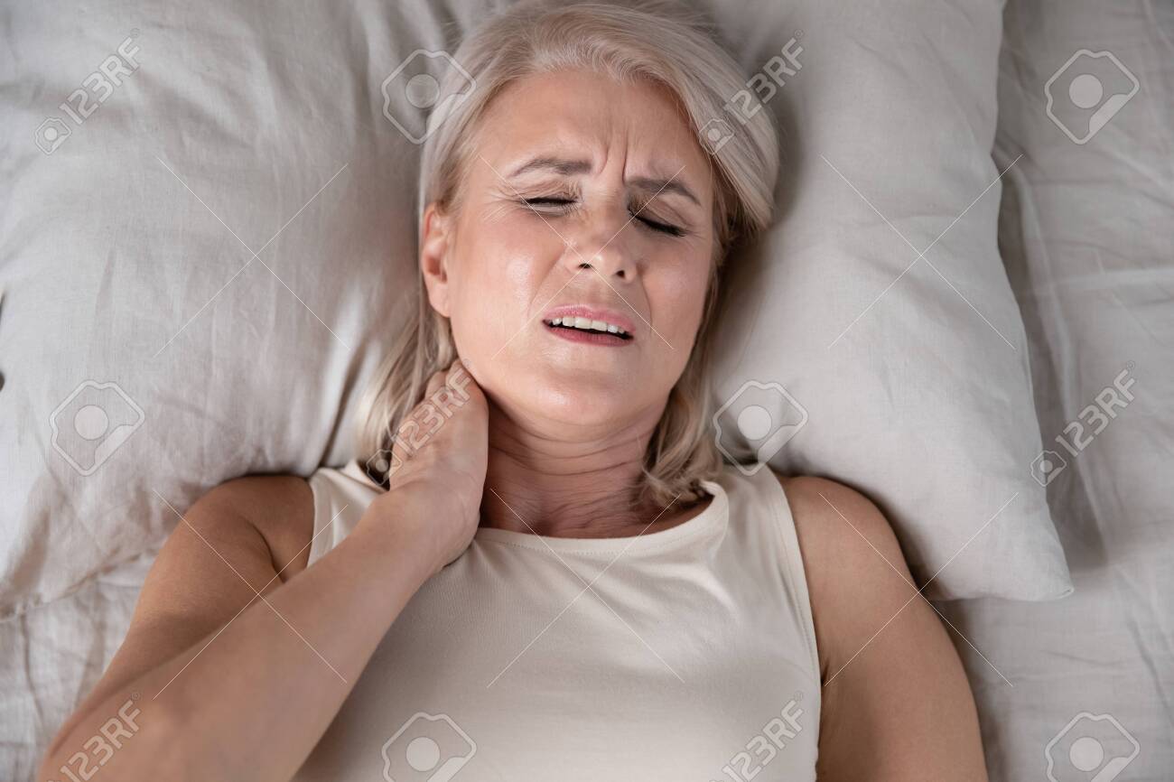 Top close up view middle-aged woman lying in bed in morning feels pain in neck after night sleep, awaken having painful sudden ache or stiffness, incorrect posture during asleep, soft mattress concept - 134588252 Top close up view middle-aged woman lying in bed in morning feels pain in neck after night sleep, awaken having painful sudden ache or stiffness, incorrect posture during asleep, soft mattress concept - 134588252