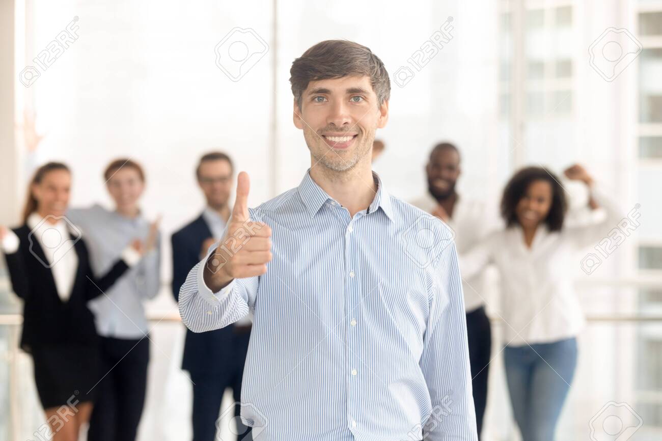 Happy Caucasian man employee or leader stand front show thumbs up recommending company service, smiling male client look at camera give recommendation, excited team support motivate at background - 137893707 Happy Caucasian man employee or leader stand front show thumbs up recommending company service, smiling male client look at camera give recommendation, excited team support motivate at background - 137893707
