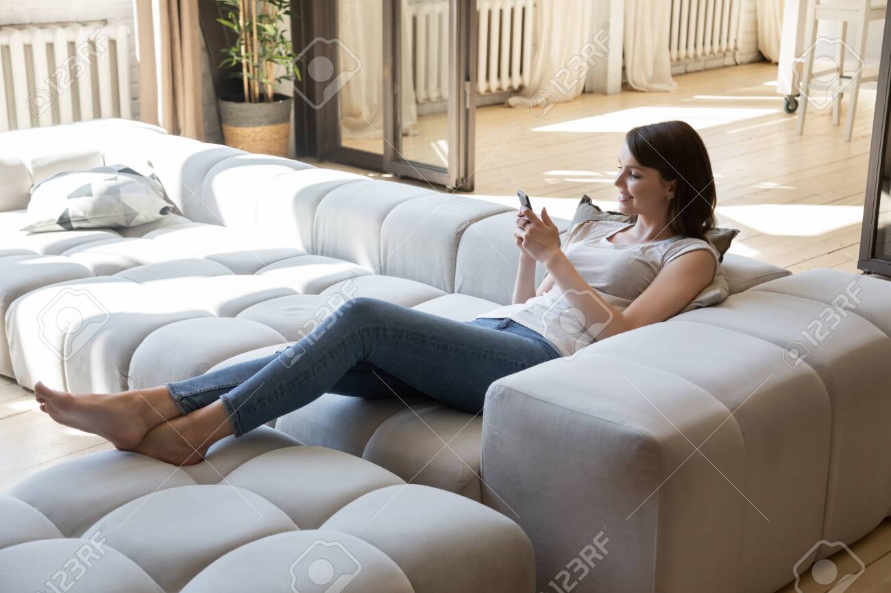 Happy Millennial Girl Lying Relaxing On Modern Comfortable Sofa Stock Photo